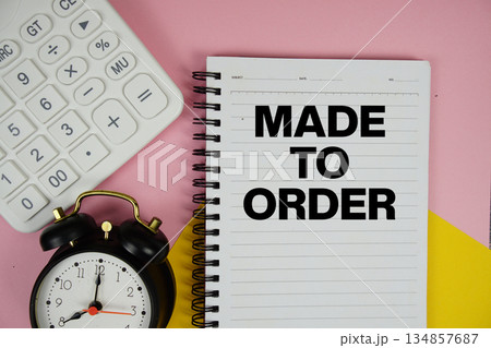 Made to Order text written on notepad with calculator and alarm clock on pink background 134857687