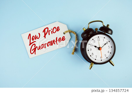 Low Price Guarantee text on price tag with alarm clock on blue background Low Price Guarantee text on price tag with alarm clock on blue background 134857724