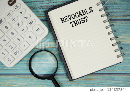 Revocable Trust text on notepad with magnifying glass and calculator on wooden background Revocable Trust text on notepad with magnifying glass and calculator on wooden background 134857844