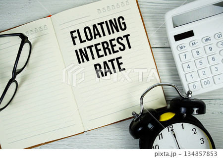 Floating Interest Rate text on notepad with alarm clock, magnifying glass and calculator on wooden background 134857853