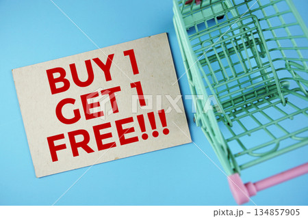 Buy 1, Get 1 Free text on paper card with trolley shopping cart on blue background Buy 1, Get 1 Free text on paper card with trolley shopping cart on blue background 134857905