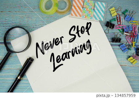 Never Stop Learning text on a paper surrounded by office supplies and magnifying glass on a blue wooden surface Never Stop Learning text on a paper surrounded by office supplies and magnifying glass on a blue wooden surface 134857959