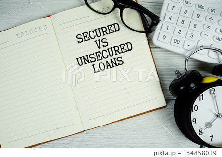Secured vs Unsecured Loans text on notepad with alarm clock, magnifying glass and calculator on wooden background 134858019