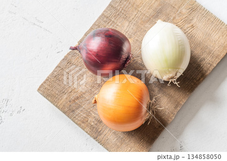 Three whole onions on rustic board showing red, yellow, and white varieties 134858050