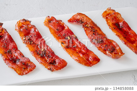 Billionaire bacon strips glazed with pepper and chili flakes on minimalist plate Billionaire bacon strips glazed with pepper and chili flakes on minimalist plate 134858088