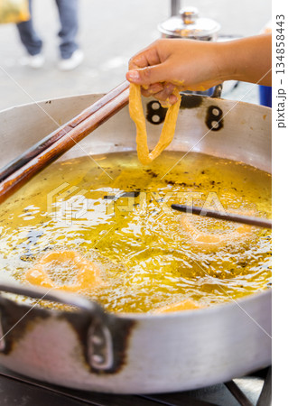 A woman is cooking picarones in a pan. A woman is cooking picarones in a pan. 134858443