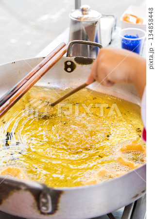 A woman is cooking picarones in a pan. A woman is cooking picarones in a pan. 134858448