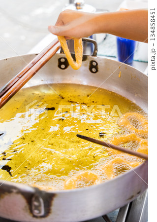 A woman is cooking picarones in a pan. A woman is cooking picarones in a pan. 134858451