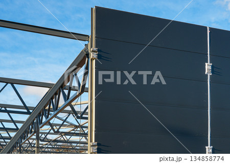 Steel frame structure with sandwich wall panels on modern industrial warehouse under construction Steel frame structure with sandwich wall panels on modern industrial warehouse under construction 134858774