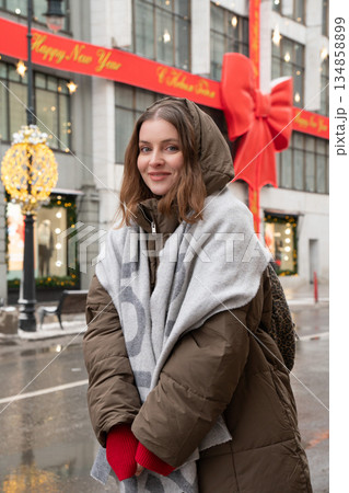 Woman in winter coat and scarf stands on wet street near decorated facade and entrance area of the TSUM Department Store during the New Year season Woman in winter coat and scarf stands on wet street near decorated facade and entrance area of the TSUM Department Store during the New Year season 134858899