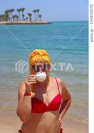Girl drinking coffee standing on beach during vacation. Woman enjoying holidays 134859478