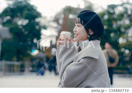 屋外で腰掛けてコーヒーを飲む30代女性の全身ライフスタイル 屋外で腰掛けてコーヒーを飲む30代女性の全身ライフスタイル 134860719