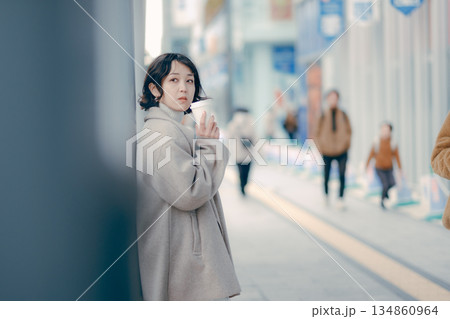 バス停でコーヒーを飲みながら待つ30代女性のポートレート 134860964
