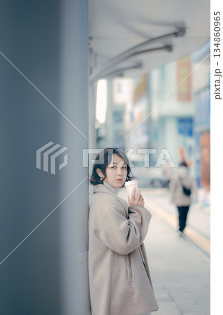 バス停でコーヒーを飲みながら待つ30代女性のポートレート 134860965