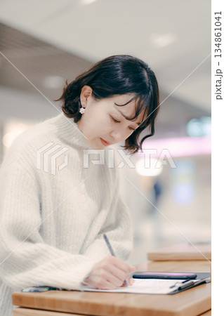街中でメモを書きながら作業する30代女性 街中でメモを書きながら作業する30代女性 134861041