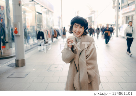 街中でコーヒーを持ちながら歩く女性 134861101
