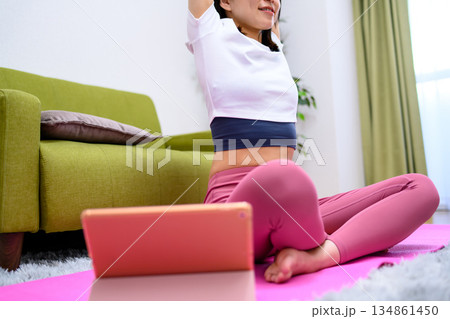 タブレットでYouTube動画を見ながら自宅で柔軟、ヨガをする若い女性 ヨガウェア タブレットでYouTube動画を見ながら自宅で柔軟、ヨガをする若い女性 ヨガウェア 134861450