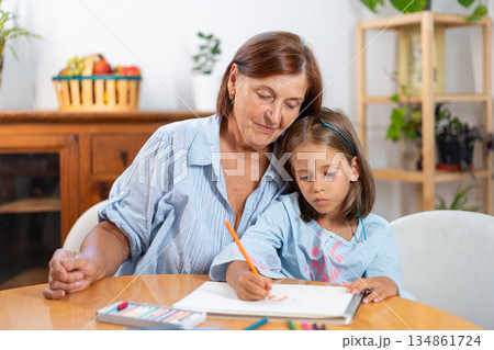 Grandmother watching girl drawing with colored Grandmother watching girl drawing with colored 134861724