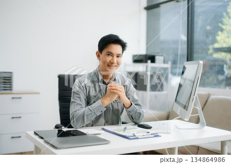Young attractive Asian man smiling thinking planning writing in notebook, tablet and laptop Young attractive Asian man smiling thinking planning writing in notebook, tablet and laptop 134864986