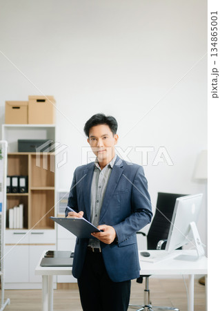 Young attractive Asian man smiling thinking planning writing in notebook, tablet and laptop 134865001