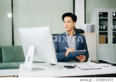 Asian businessman working with working notepad, tablet and laptop documents talking on the smartphone, tablet and laptop Asian businessman working with working notepad, tablet and laptop documents talking on the smartphone, tablet and laptop 134865053