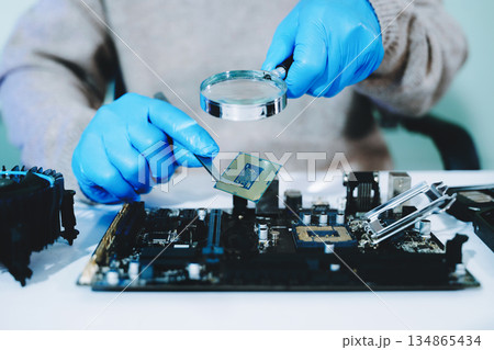 Closeup of technician inspecting CPU with magnifying glass before installing it on motherboard. Concept: repair, upgrade, precision tech work Closeup of technician inspecting CPU with magnifying glass before installing it on motherboard. Concept: repair, upgrade, precision tech work 134865434
