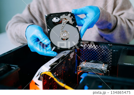 Closeup of technician with gloves holding opened hard drive above computer case, symbolizing data storage, recovery, computer repair, and IT service. 134865475