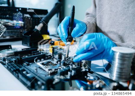 Closeup of technician soldering a computer motherboard with precision tools, showcasing electronics repair, hardware maintenance, and modern technology Closeup of technician soldering a computer motherboard with precision tools, showcasing electronics repair, hardware maintenance, and modern technology 134865494