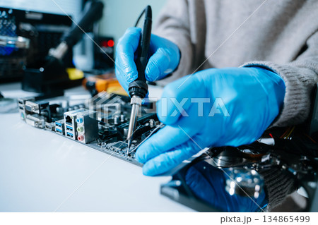 Computer technician in gloves safely repairing desktop hardware. Closeup view of hands fixing GPU and motherboard inside open PC case. Perfect for tech 134865499