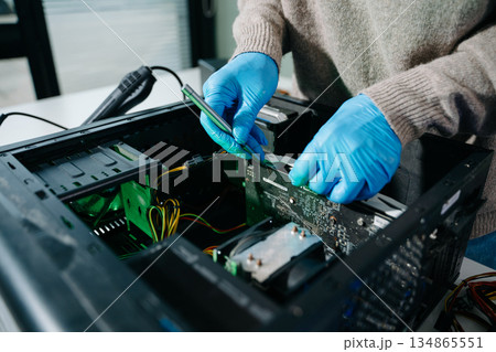 Computer technician in gloves safely repairing desktop hardware. Close-up view of hands fixing GPU and motherboard inside open PC case. Perfect for tech and repair concepts. Computer technician in gloves safely repairing desktop hardware. Close-up view of hands fixing GPU and motherboard inside open PC case. Perfect for tech and repair concepts. 134865551
