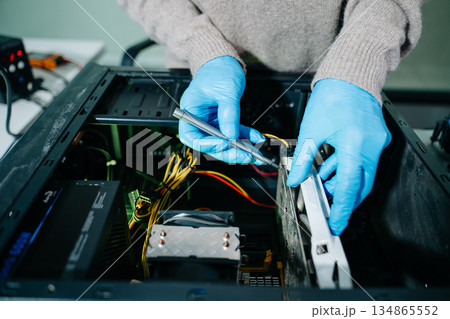 Computer technician in gloves safely repairing desktop hardware. Close-up view of hands fixing GPU and motherboard inside open PC case. Perfect for tech and repair concepts. 134865552