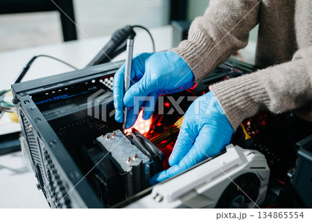 Computer technician in gloves safely repairing desktop hardware. Close-up view of hands fixing GPU and motherboard inside open PC case. Perfect for tech and repair concepts. 134865554