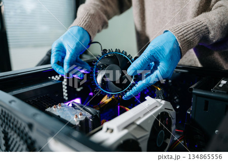 Closeup of technician in gloves holding CPU cooler and heat gun over desktop PC. Ideal image for computer repair, cooling system, and hardware Closeup of technician in gloves holding CPU cooler and heat gun over desktop PC. Ideal image for computer repair, cooling system, and hardware 134865556
