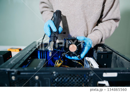 Closeup of technician in gloves holding CPU cooler and heat gun over desktop PC. Ideal image for computer repair, cooling system, and hardware Closeup of technician in gloves holding CPU cooler and heat gun over desktop PC. Ideal image for computer repair, cooling system, and hardware 134865560