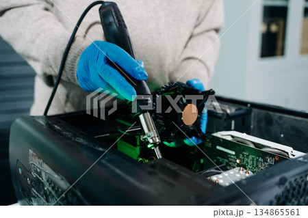 Closeup of technician in gloves holding CPU cooler and heat gun over desktop PC. Ideal image for computer repair, cooling system, and hardware Closeup of technician in gloves holding CPU cooler and heat gun over desktop PC. Ideal image for computer repair, cooling system, and hardware 134865561