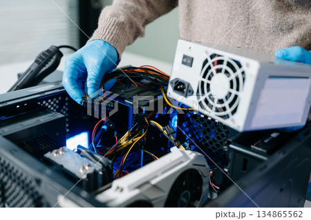 Computer technician in gloves safely repairing desktop hardware. Close-up view of hands fixing GPU and motherboard inside open PC case. Perfect for tech and repair concepts. 134865562