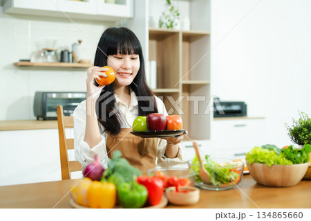 Asian woman prepares healthy salad with fresh vegetables in a modern kitchen. Clean, vibrant, and perfect for nutrition, lifestyle, or home cooking concepts. 134865660