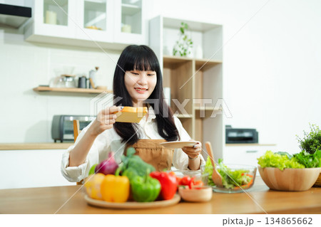 Asian woman prepares healthy salad with fresh vegetables in a modern kitchen. Clean, vibrant, and perfect for nutrition, lifestyle, or home cooking concepts. Asian woman prepares healthy salad with fresh vegetables in a modern kitchen. Clean, vibrant, and perfect for nutrition, lifestyle, or home cooking concepts. 134865662