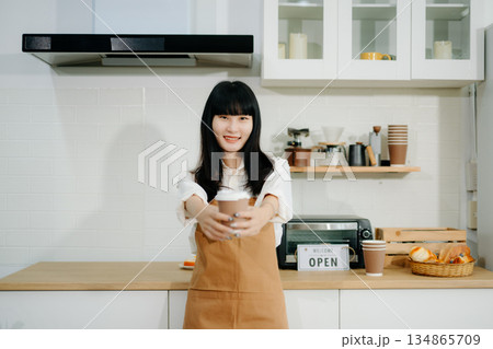 Young Asian woman coffee shop owner holding notepad and digital tablet ready to receive orders in cafe restaurant. 134865709