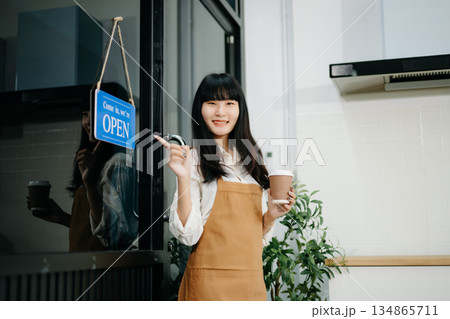 Young female entrepreneur hanging a welcome sign in front of a coffee shop. Beautiful waitress Young female entrepreneur hanging a welcome sign in front of a coffee shop. Beautiful waitress 134865711
