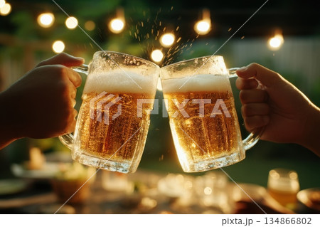 Two Hands Clinking Large Frosty Beer Mugs Overflowing with Golden Froth in Outdoor Setting Two Hands Clinking Large Frosty Beer Mugs Overflowing with Golden Froth in Outdoor Setting 134866802