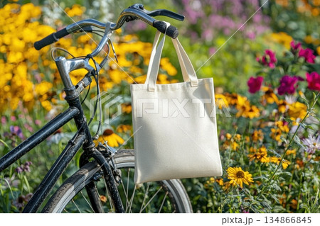 Professional Mockup of White Tote Bag Hanging on Bicycle in Floral Setting 134866845