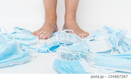 Feet standing on a chaotic pile of discarded medical face masks, symbolizing the environmental impact of single-use items and the urgent need for sustainable practices in healthcare and personal 134867267