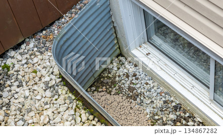 Exterior view of a drainage system with gravel and metal edging, showcasing water management features and landscaping elements for home improvement Exterior view of a drainage system with gravel and metal edging, showcasing water management features and landscaping elements for home improvement 134867282