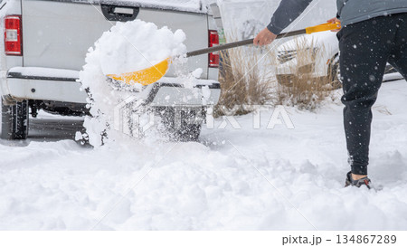 Snow cleaning service worker shoveling snow from driveway near parked truck, showcasing winter maintenance and outdoor labor efforts 134867289