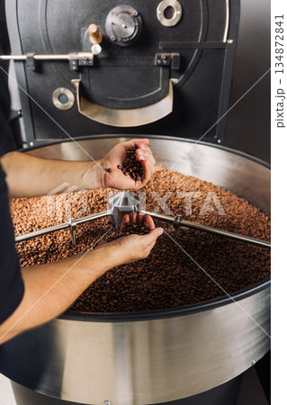 Male hands with fresh roasted coffee beans, checking the quality above the machine drum 134872841
