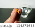 指先に錠剤、奥に水（服薬イメージ）  タグ案 134873633