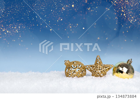 Christmas tree baubles on blue background with white snow and golden lights. Festive winter holiday background. Design with copy space for greeting card, text, advertising, banner, invitation 134873884