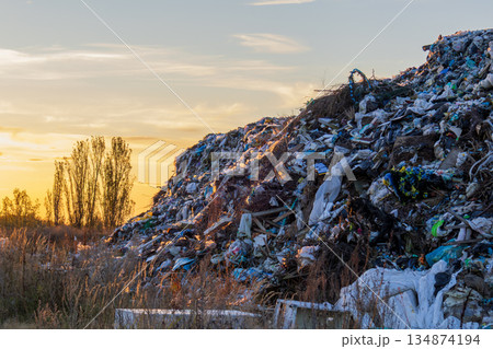 Large piles of garbage rise in the background as the sun sets, casting an orange glow over a landfill in a rural area Large piles of garbage rise in the background as the sun sets, casting an orange glow over a landfill in a rural area 134874194