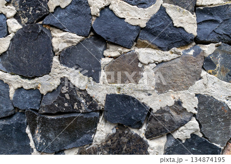 Close view of a stone wall with different shapes and colors of rock pieces fitted together in a unique pattern Close view of a stone wall with different shapes and colors of rock pieces fitted together in a unique pattern 134874195